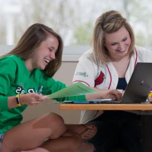 two girls smiling in front of a laptop