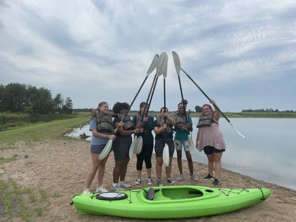 Upward Bound students point oars together over green canoe